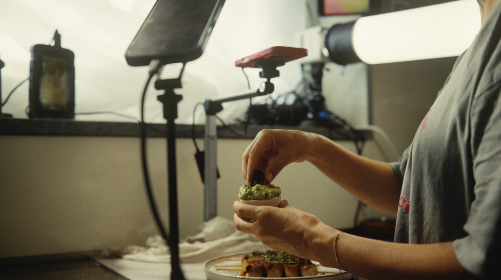 Hände setzen Guacamole auf eine Schnitte, daneben Rig, Dauerlicht und Monitor